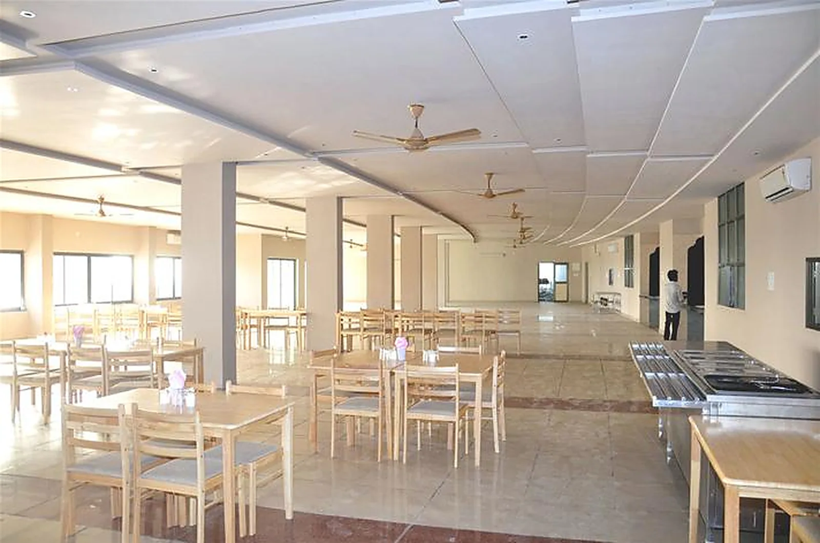 The guest house dining hall with wooden tables and chairs and a service counter along the wall
