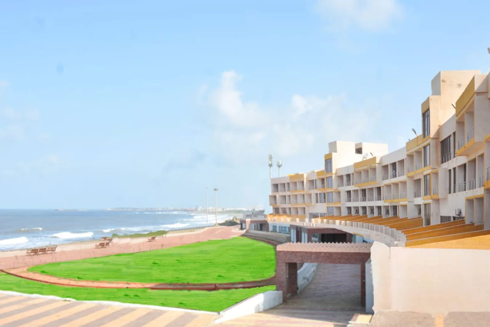 Sagar Darshan Guest House seen from its sea front lawn: a long cream four storey building behind a green lawn, with the Arabian Sea on the right