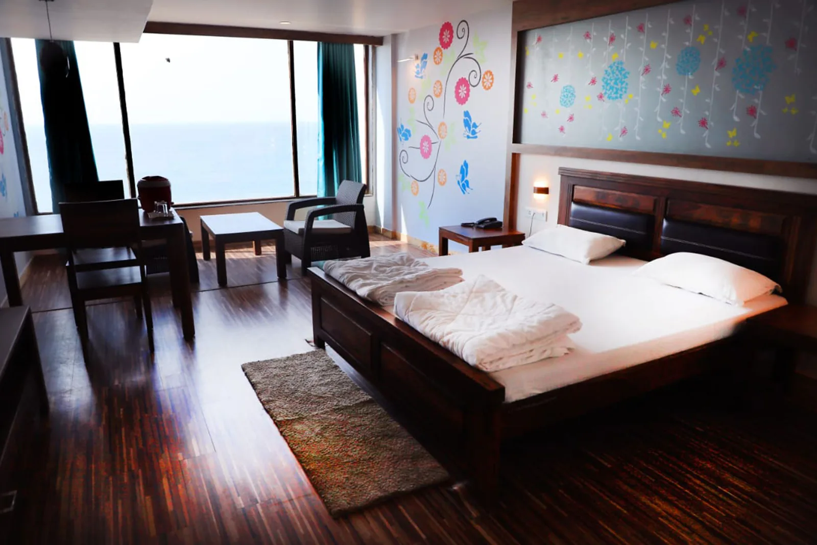 Suite room with a bed, a seating area, a wooden floor and sea facing glazing